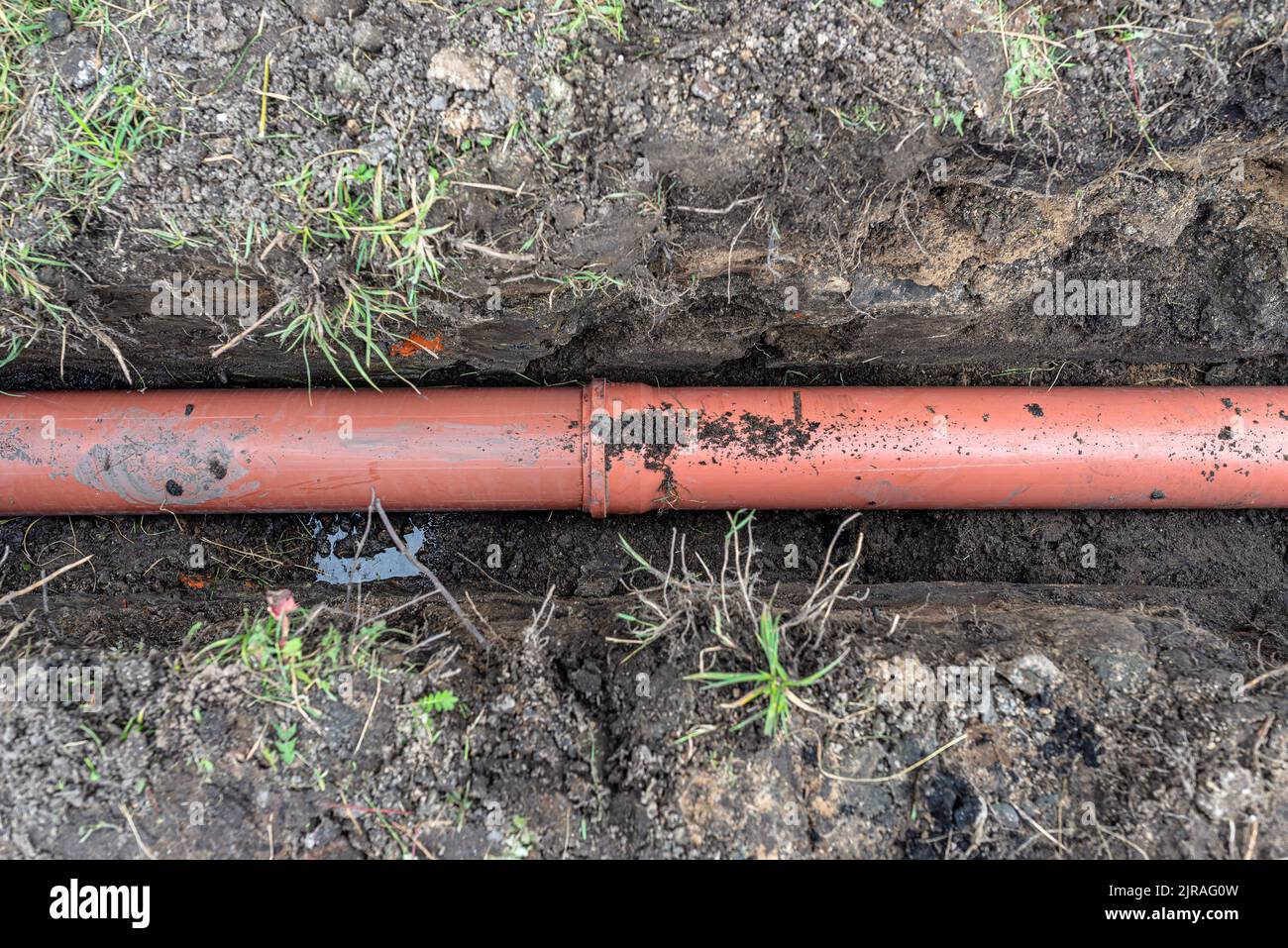 Un tubo di plastica arancione proveniente da un serbatoio settico del diametro di 160 mm giacente in un fosso. Foto Stock