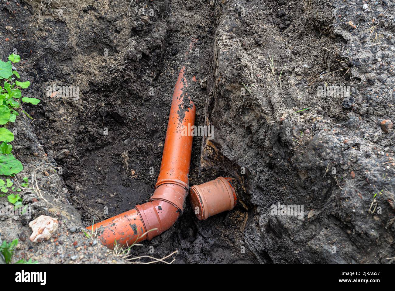 Un tubo di plastica arancione proveniente da un serbatoio settico del diametro di 160 mm giacente in un fosso, tubo cieco visibile. Foto Stock