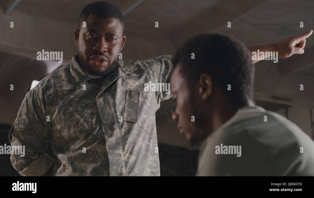 Da sotto nero militare uomo gesticulating e scolding soldato maschio su base militare Foto Stock