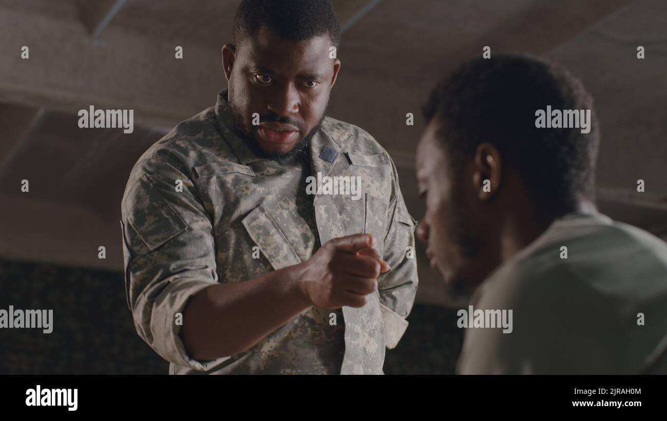 Da sotto nero militare uomo gesticulating e scolding soldato maschio su base militare Foto Stock