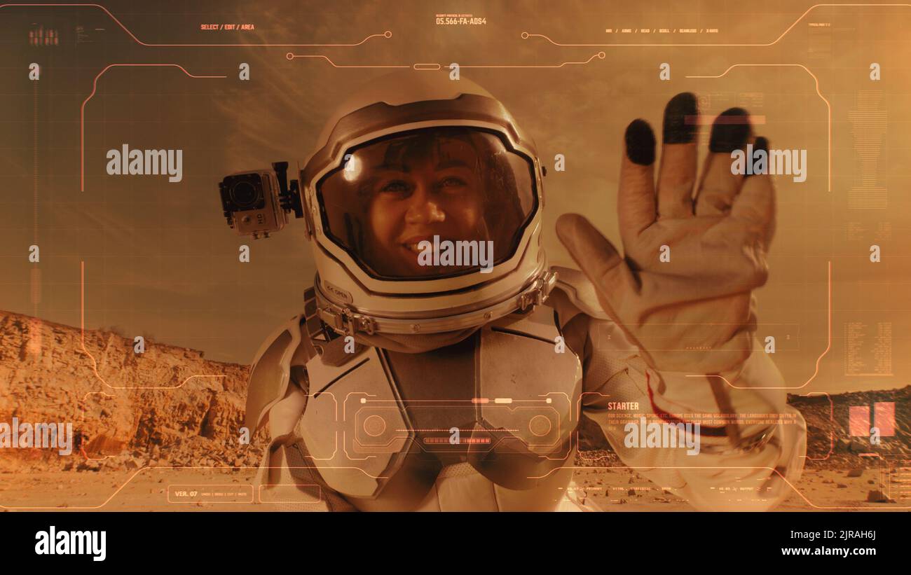 Donna nello spazio vestito agitando la mano e gestendo il pollice in su mentre parla della vita su Marte per la registrazione del diario video con l'interfaccia blu Foto Stock