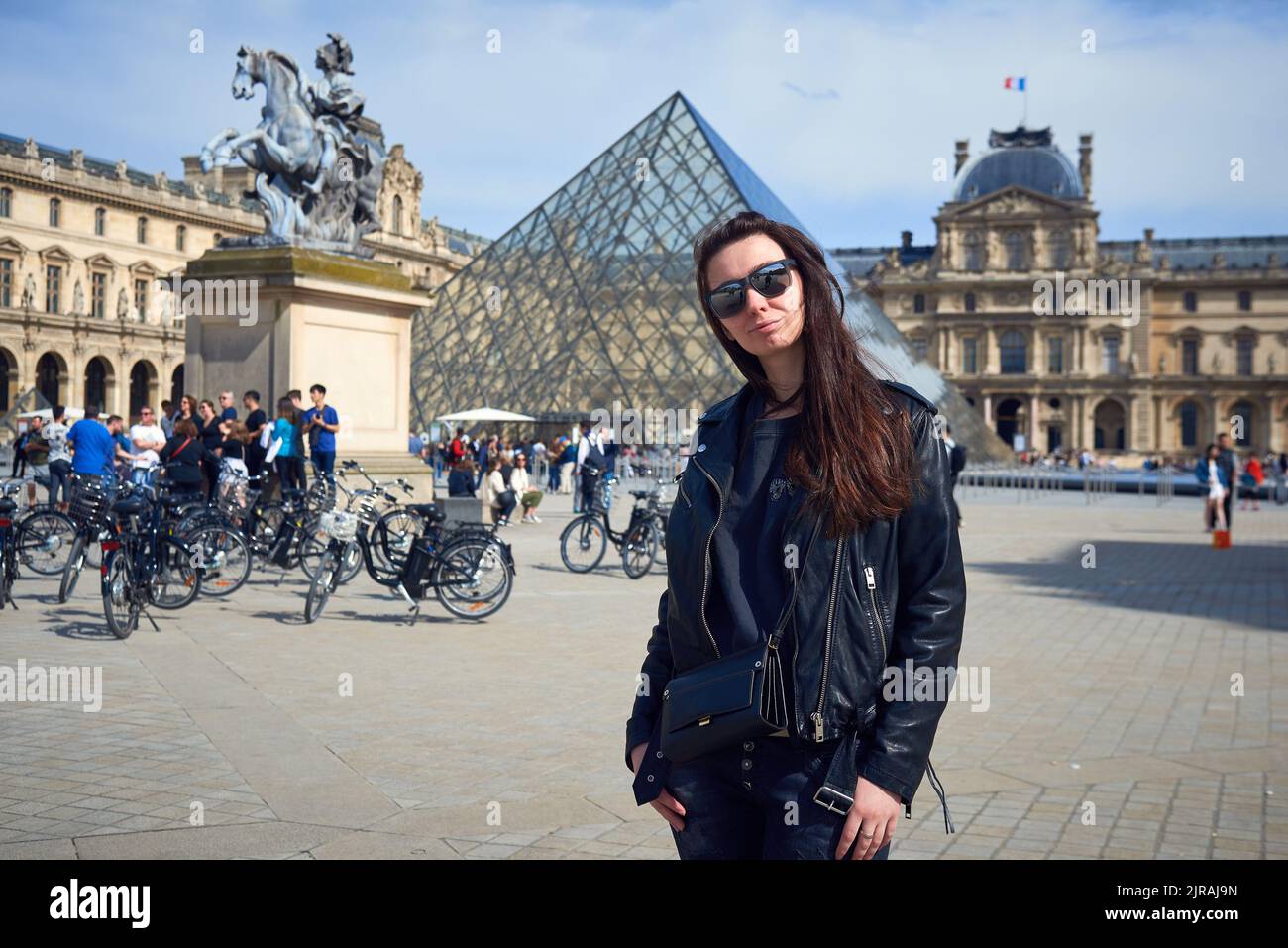 Una ragazza con giacca nera in pelle e occhiali da sole sullo sfondo di un Louvre a Parigi Foto Stock