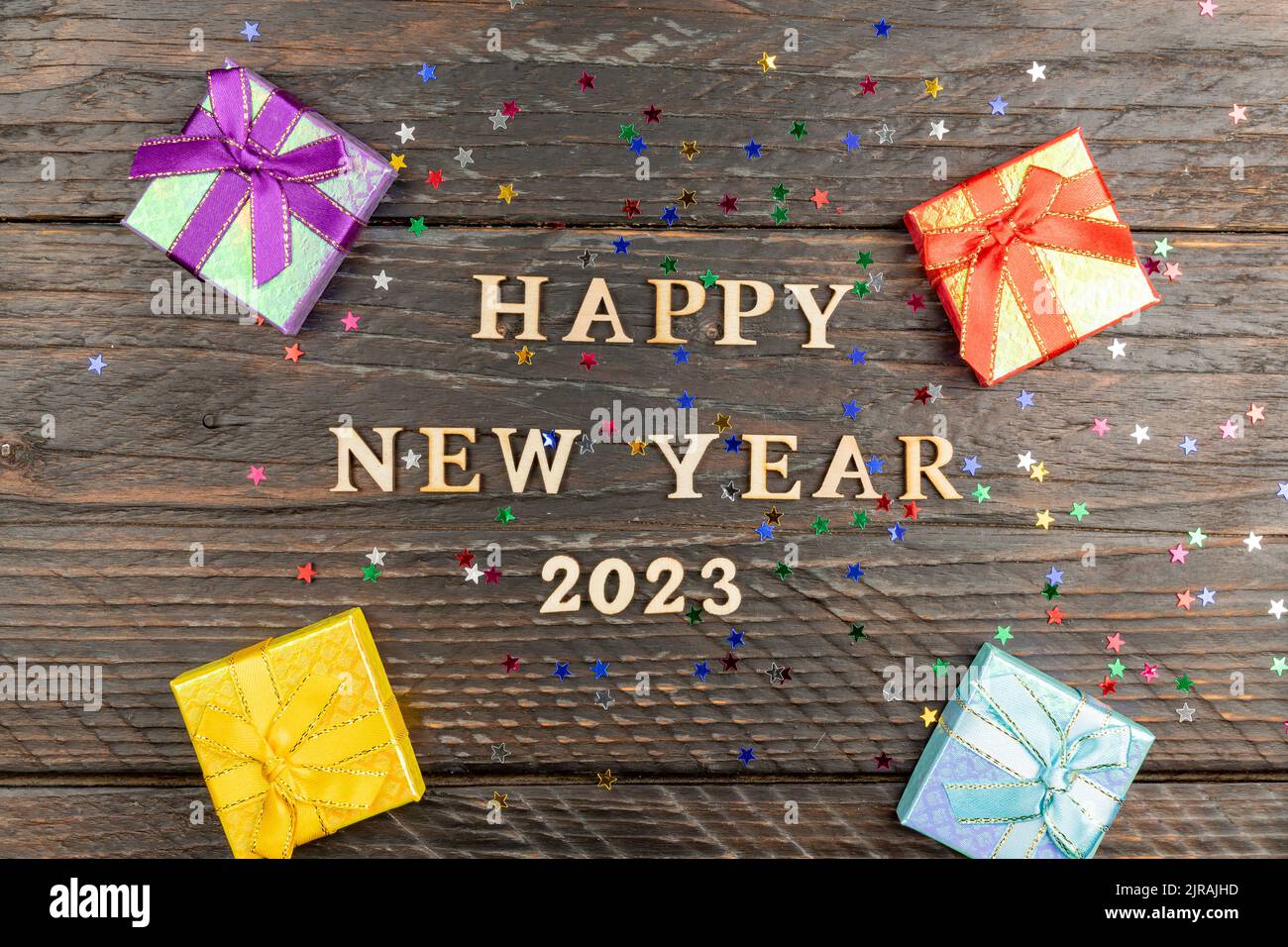 Felice anno nuovo lettere in legno su uno sfondo festoso con paillettes, stelle, confezioni regalo multicolore. Saluti, cartolina Foto Stock