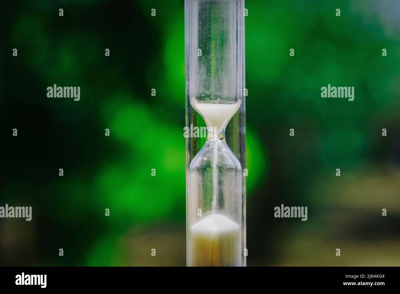 Clessidra verticale trasparente con sabbia che cade nel tempo su fondo bokeh verde. Foto Stock