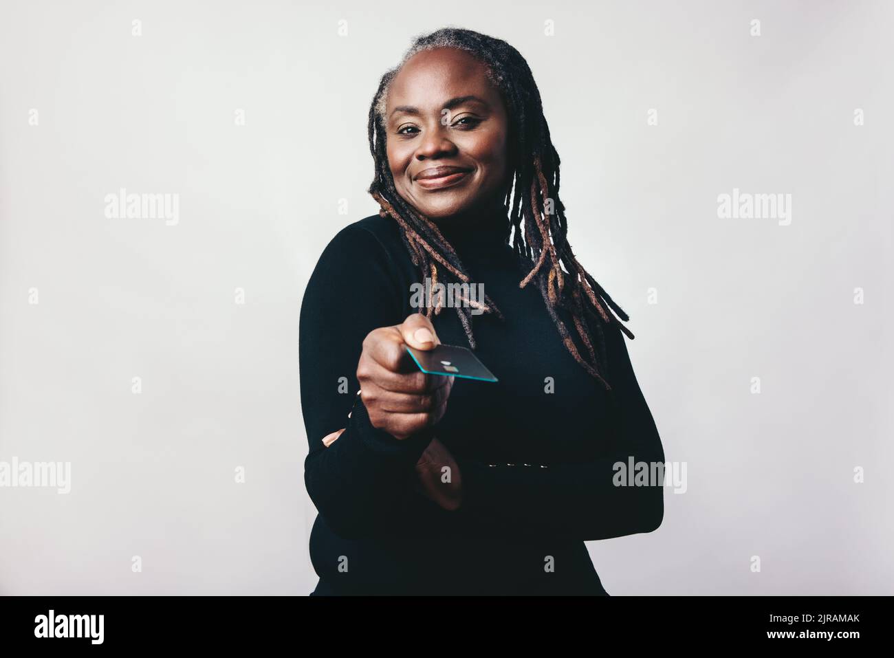 Donna felice che paga con una carta di credito. Donna matura con Dreadlocks che tiene fuori una carta di credito mentre si trova contro uno sfondo studio. Età media Foto Stock