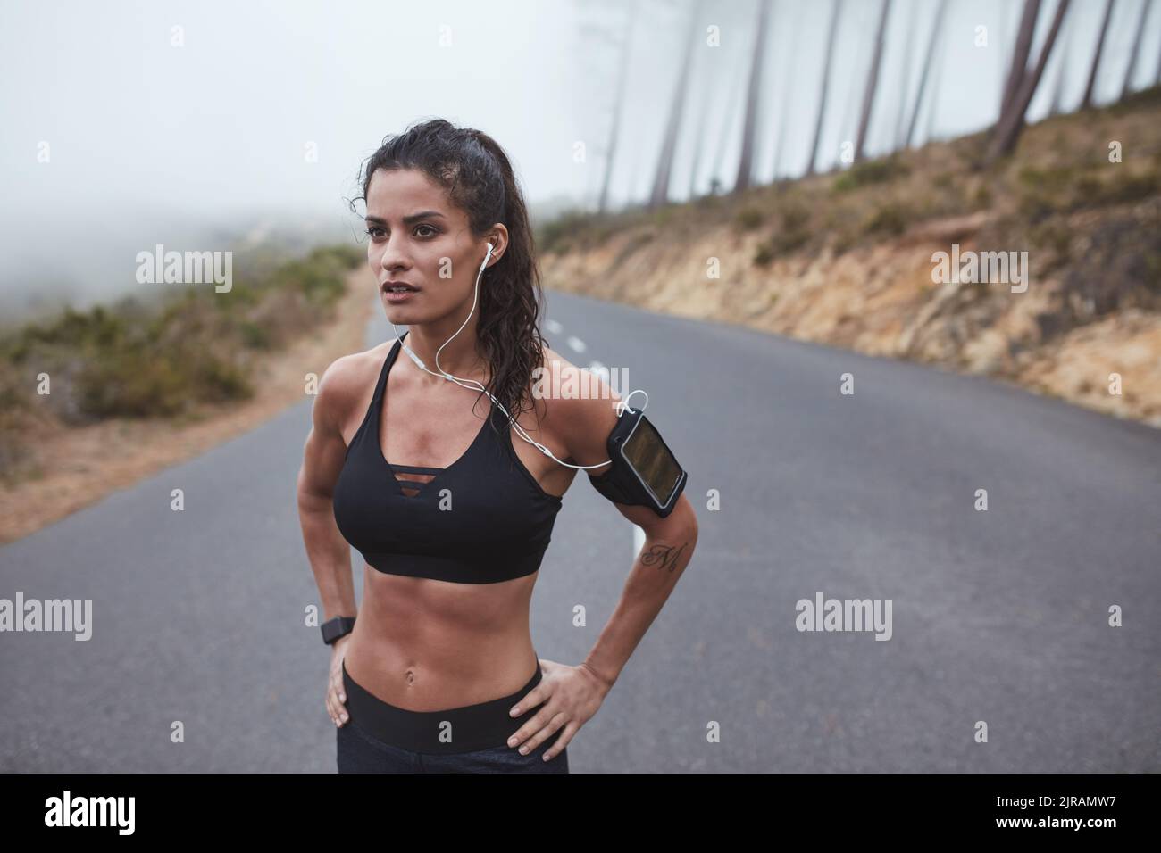 Giovane donna sportiva che ha una sessione di allenamento all'aperto su una strada misteriosa. Giovane donna atletica che ascolta musica mentre si allenano. Foto Stock