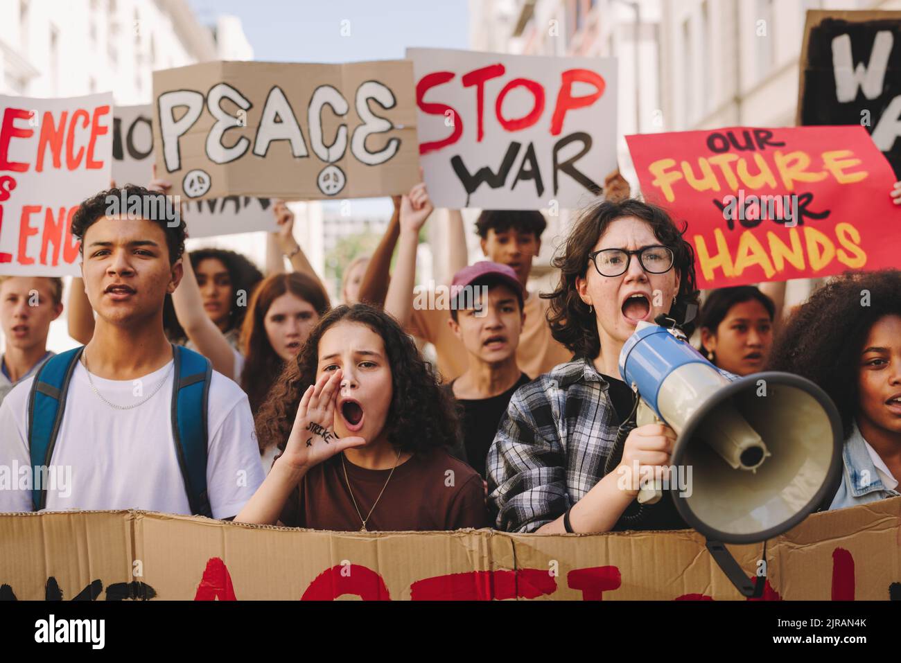 Sciopero per la pace. Gruppo di attivisti adolescenti multiculturali che cantano slogan e che alzano striscioni mentre marciano contro la guerra e la violenza. Generazione Z Foto Stock