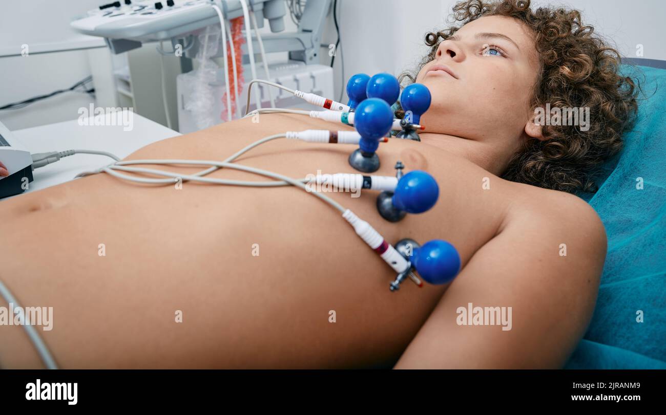 Ragazzo carino durante l'elettrocardiogramma cardiaco con sensori del vuoto sul suo corpo sdraiato sul letto in clinica medica. Elettrocardiografia per bambini Foto Stock