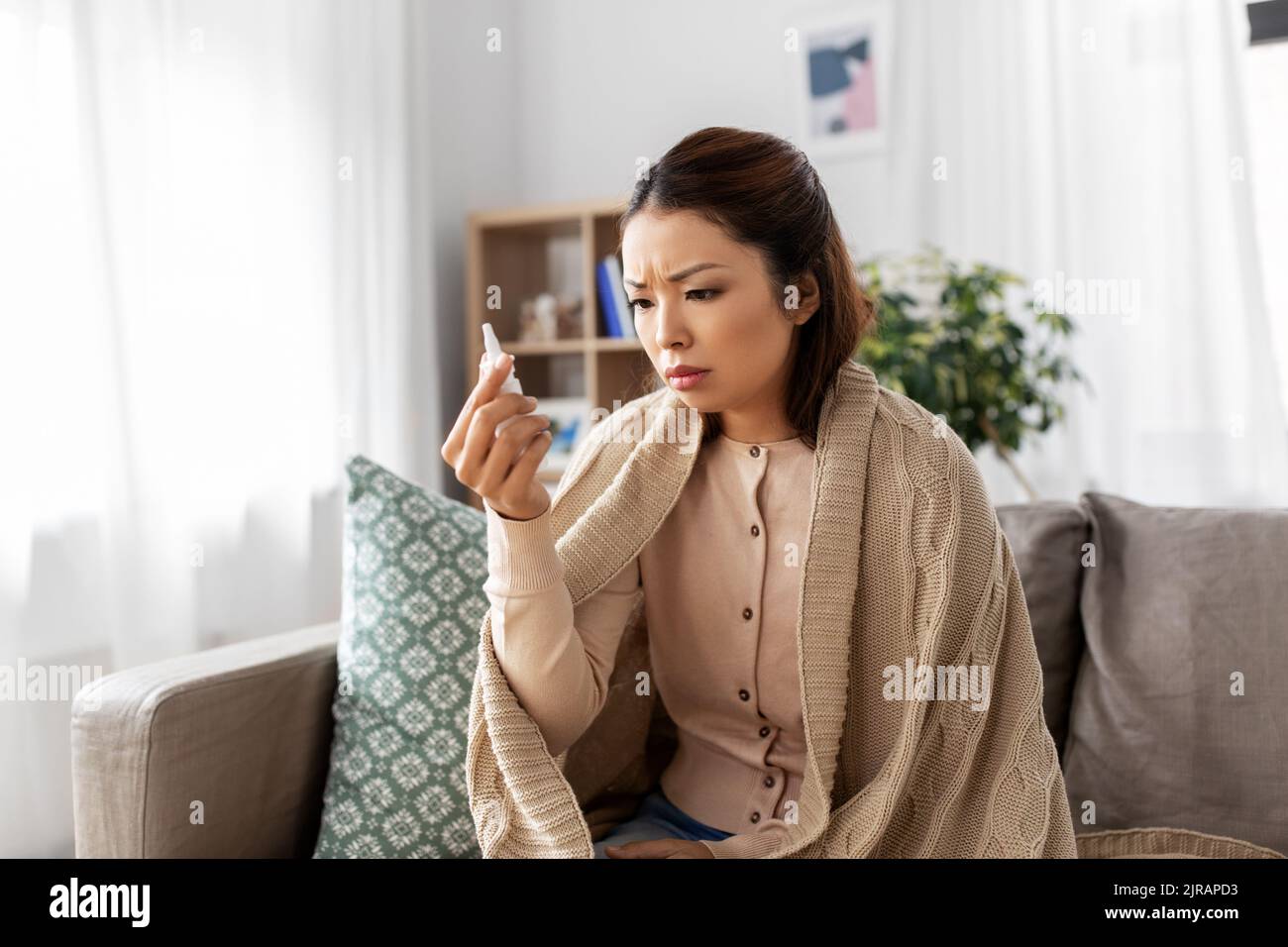 donna asiatica malata con spray nasale a casa Foto Stock