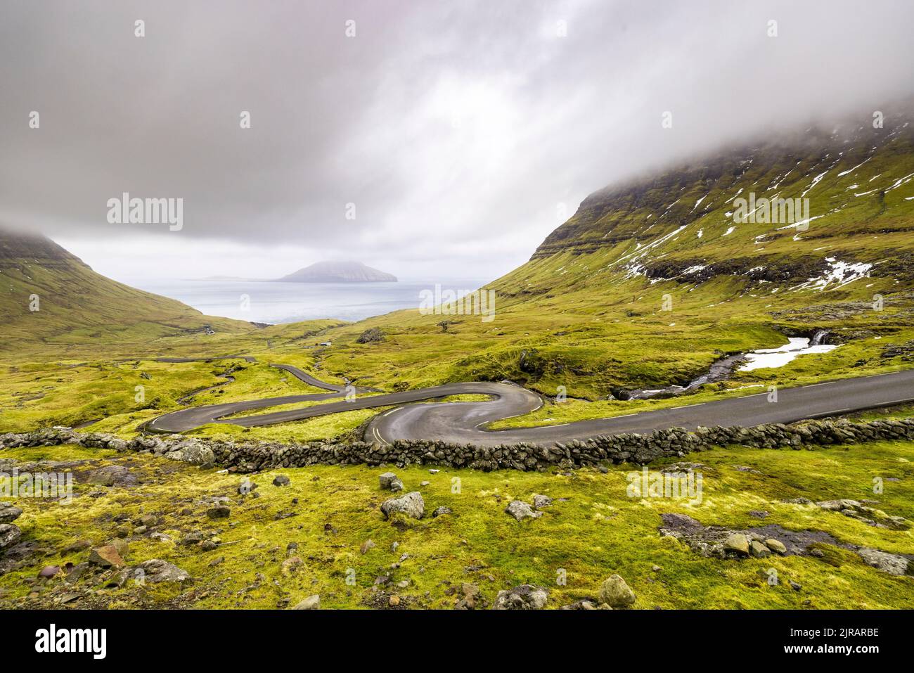 Isole Faroe, Streymoy, cielo nuvoloso su strada tortuosa Foto Stock