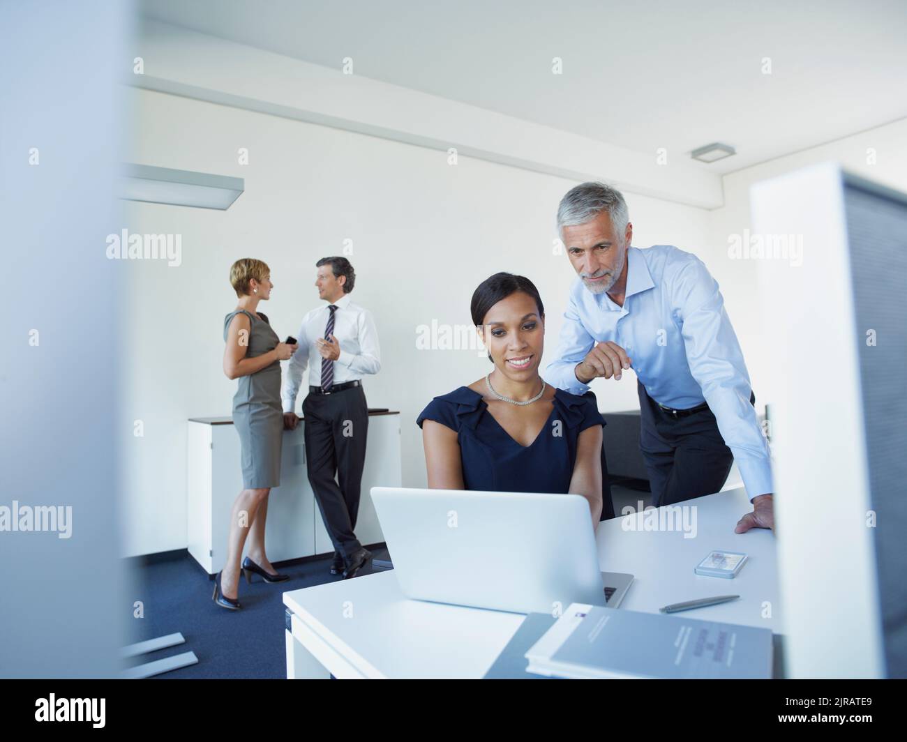 Uomo d'affari maturo e donna d'affari che usano il laptop con i colleghi che discutono in ufficio Foto Stock