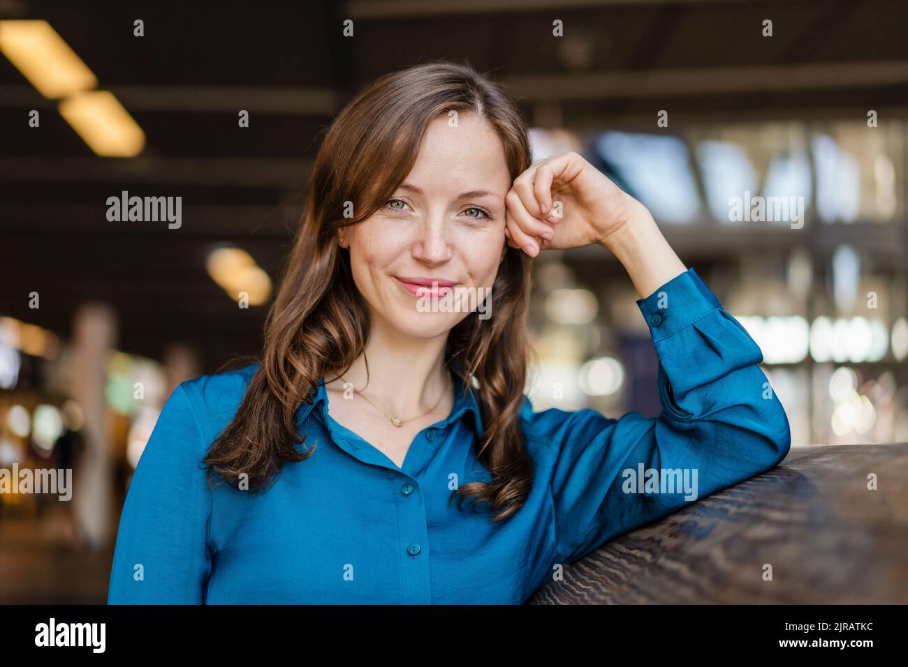 Donna sorridente che indossa una camicia blu appoggiata al muro Foto Stock
