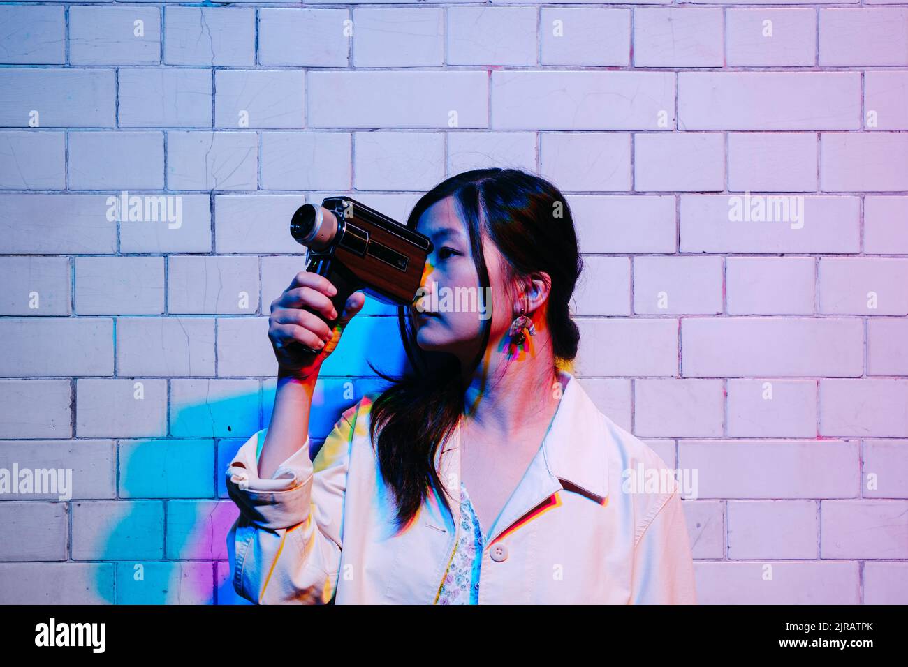 Giovane donna che filma attraverso la videocamera davanti al muro Foto Stock