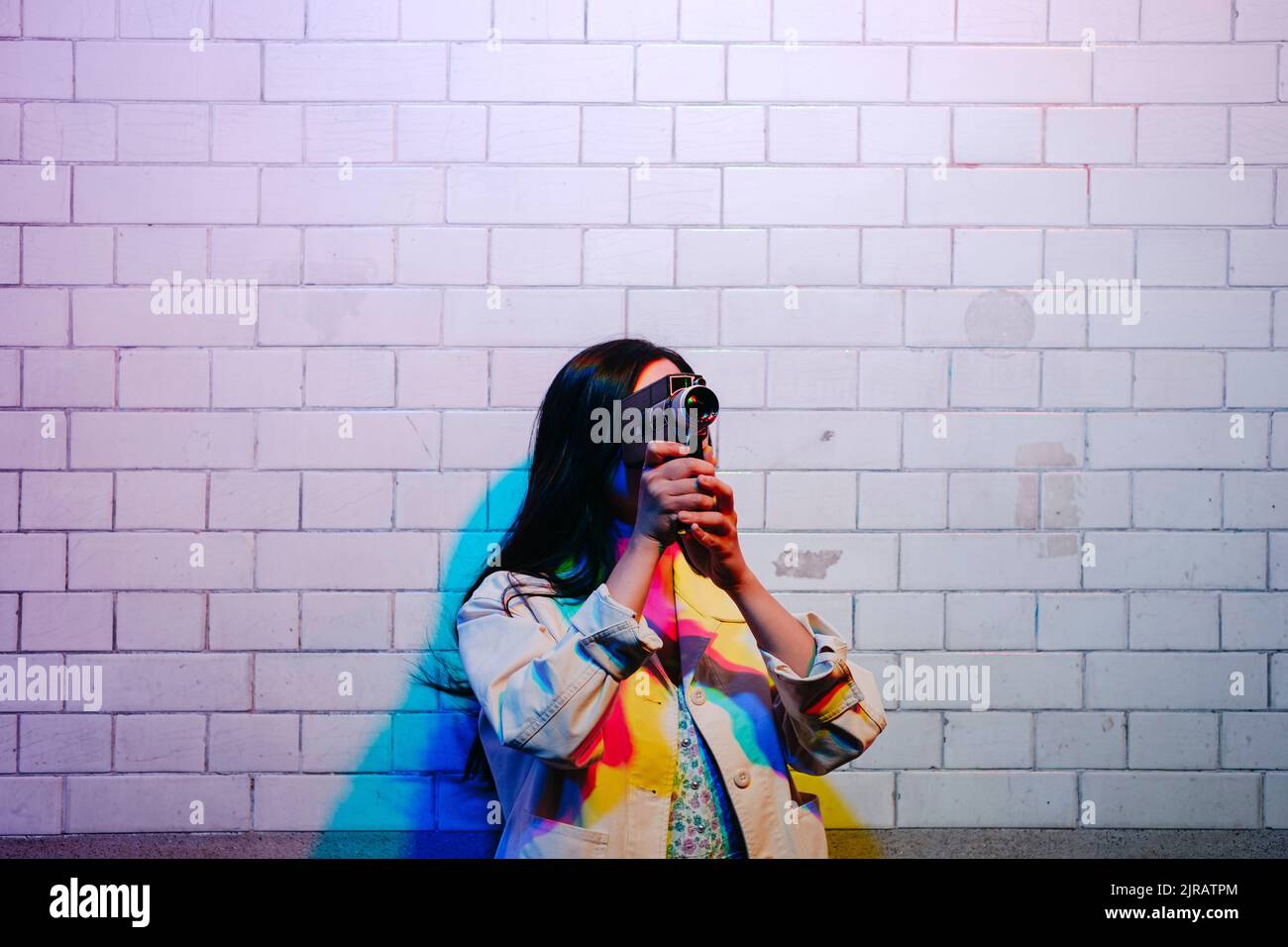 Giovane donna che filma con la videocamera davanti al muro Foto Stock