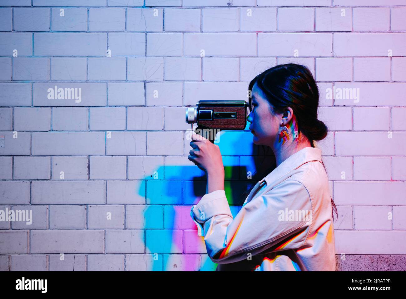 Donna che filma attraverso la videocamera davanti al muro Foto Stock