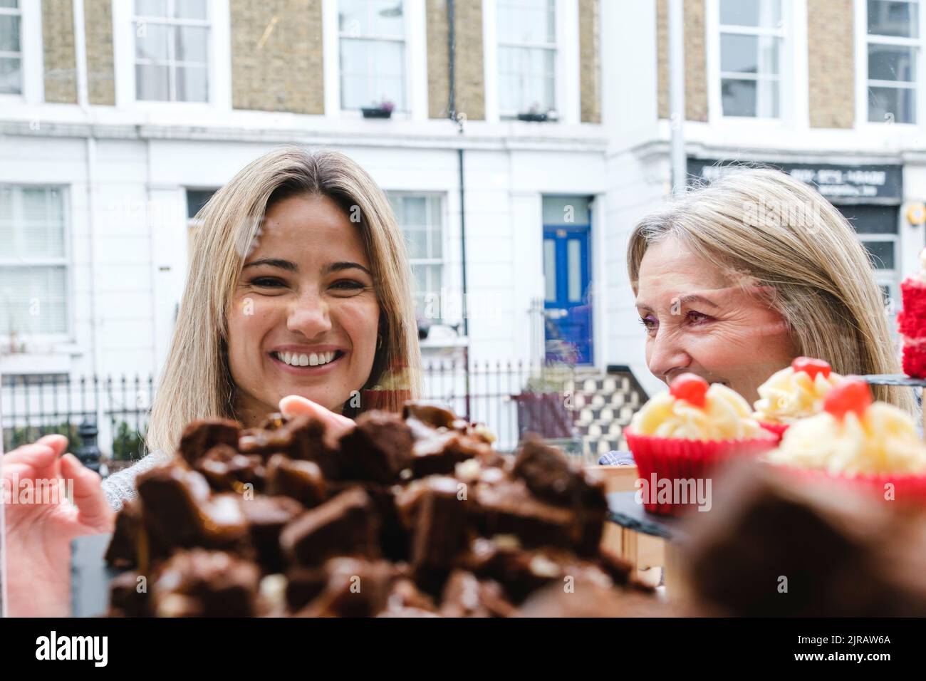 Donna sorridente che guarda il cibo dolce dalla finestra dalla madre Foto Stock