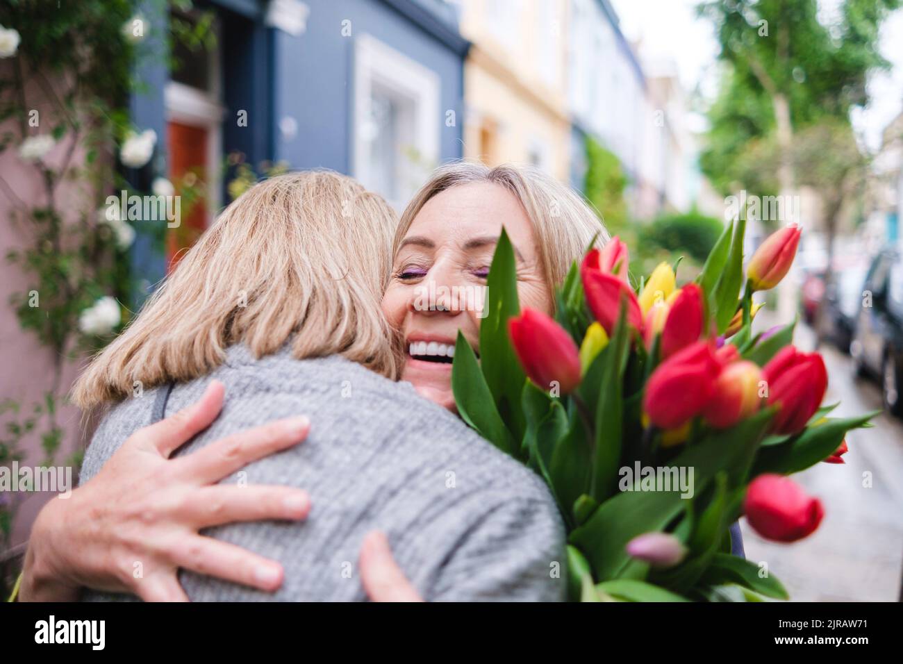 Donna anziana felice con fiori che abbracciano la figlia Foto Stock