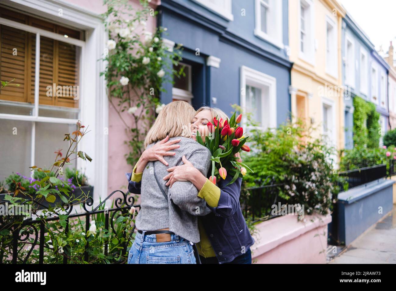 Madre e figlia con fiori di tulipano che abbracciano in città Foto Stock