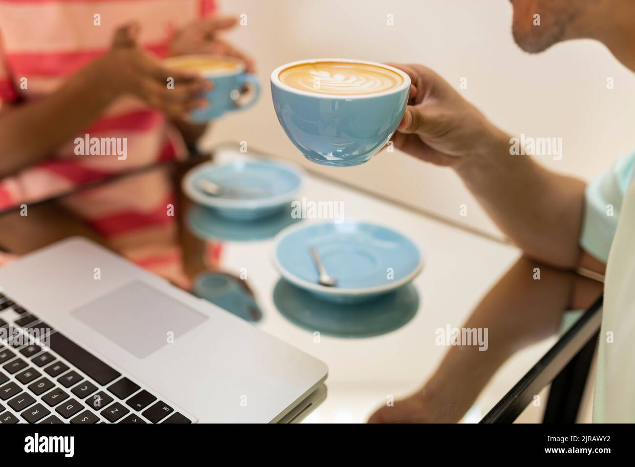 Uomo e donna che tengono tazze di cappuccino al tavolo nel caffè Foto Stock