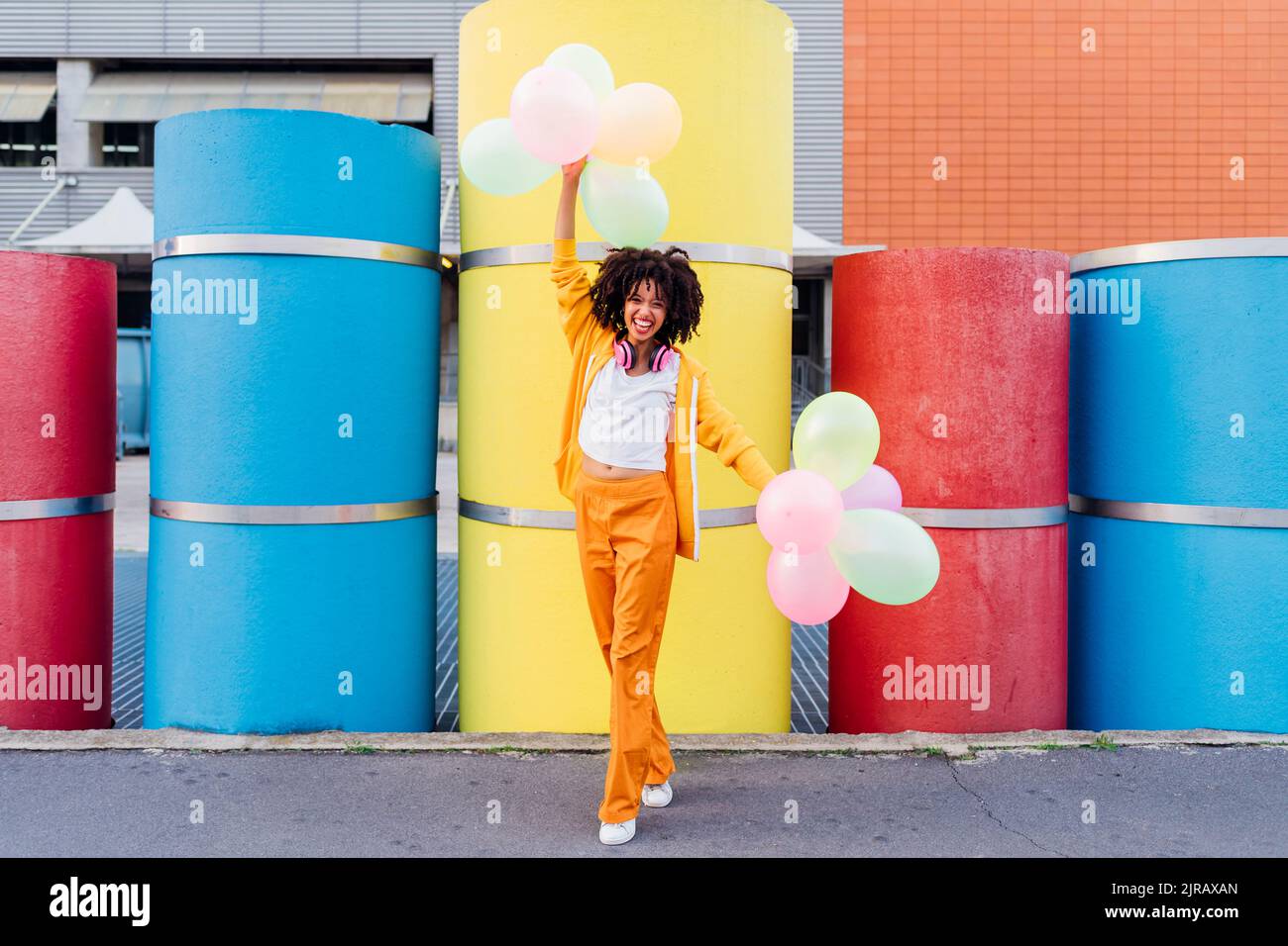 Donna felice che gioca con palloncini colorati di fronte alle pipe Foto Stock