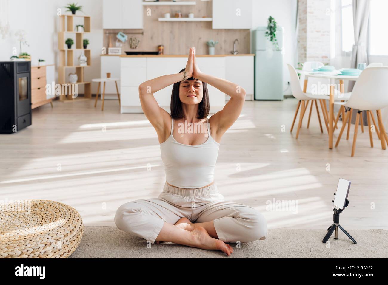 Donna che pratica lo yoga con uno smartphone sul cavalletto a casa Foto Stock