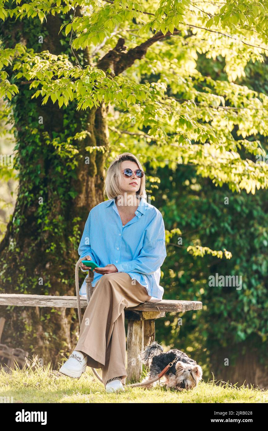 Donna matura in possesso di uno smartphone seduto sul panca da cane al parco Foto Stock
