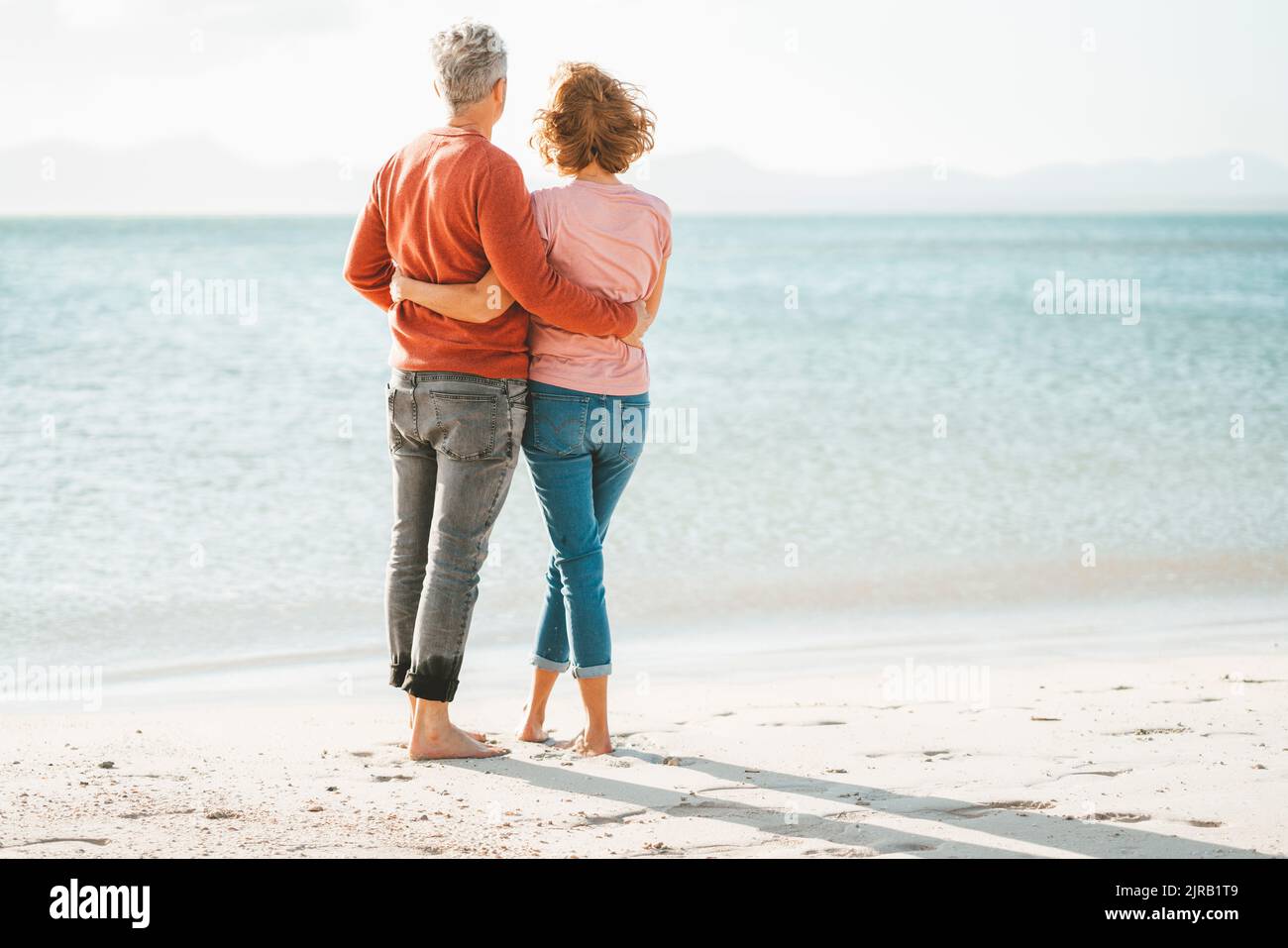 Coppia matura amorevole con le braccia intorno l'un l'altro in piedi sulla riva in spiaggia Foto Stock