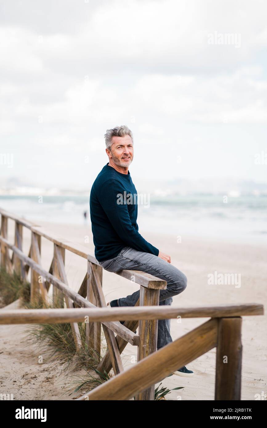 Felice uomo maturo seduto sulla ringhiera in spiaggia Foto Stock