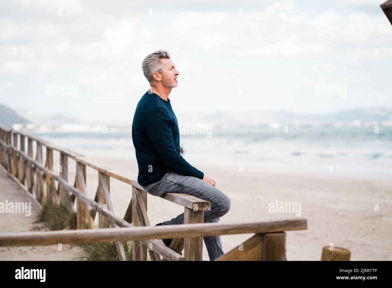 Uomo maturo e premuroso seduto sulla ringhiera in spiaggia Foto Stock