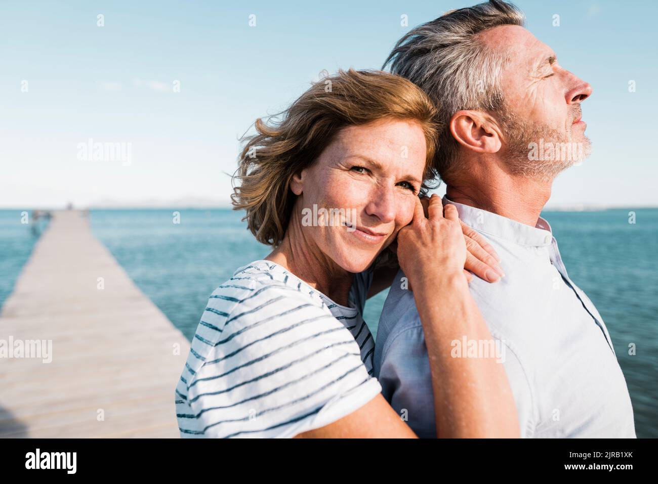 Donna matura sorridente in piedi con l'uomo al molo nelle giornate di sole Foto Stock