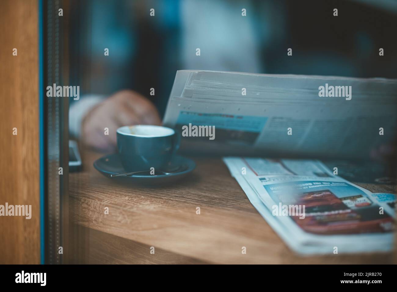 Uomo d'affari con giornali e caffè visto attraverso la finestra del caffè Foto Stock