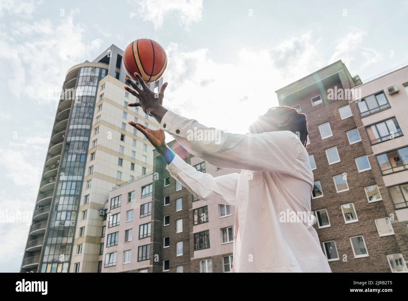 Giovane uomo che lancia il basket di fronte agli edifici nelle giornate di sole Foto Stock