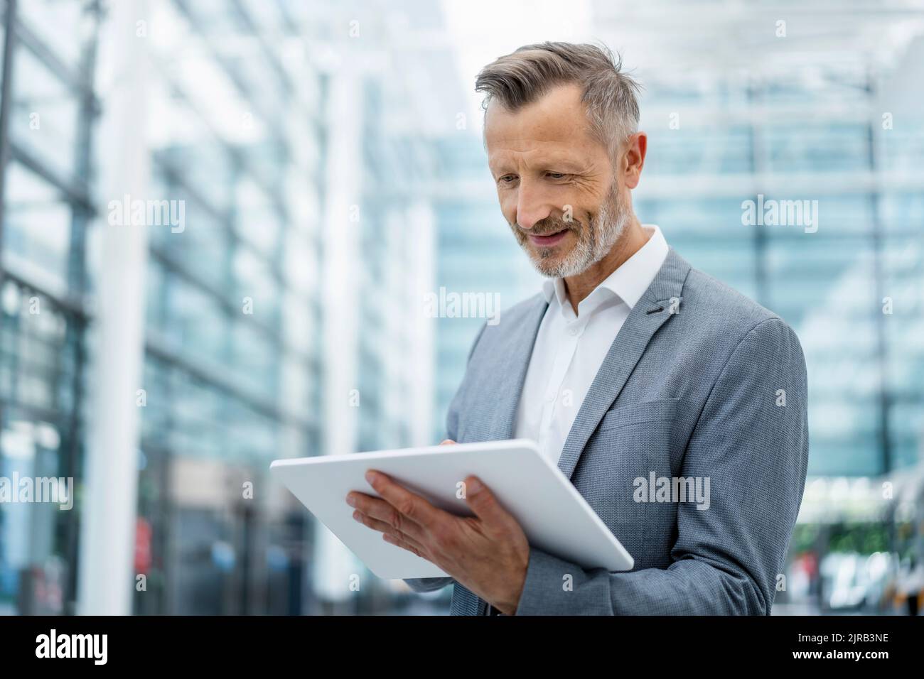 Uomo d'affari sorridente in blazer grigio utilizzando un tablet digitale Foto Stock