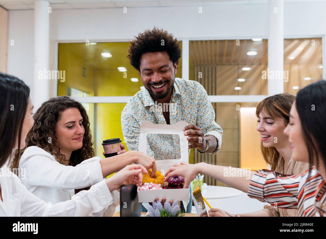 Uomo d'affari che consegna le ciambelle ai colleghi in ufficio Foto Stock