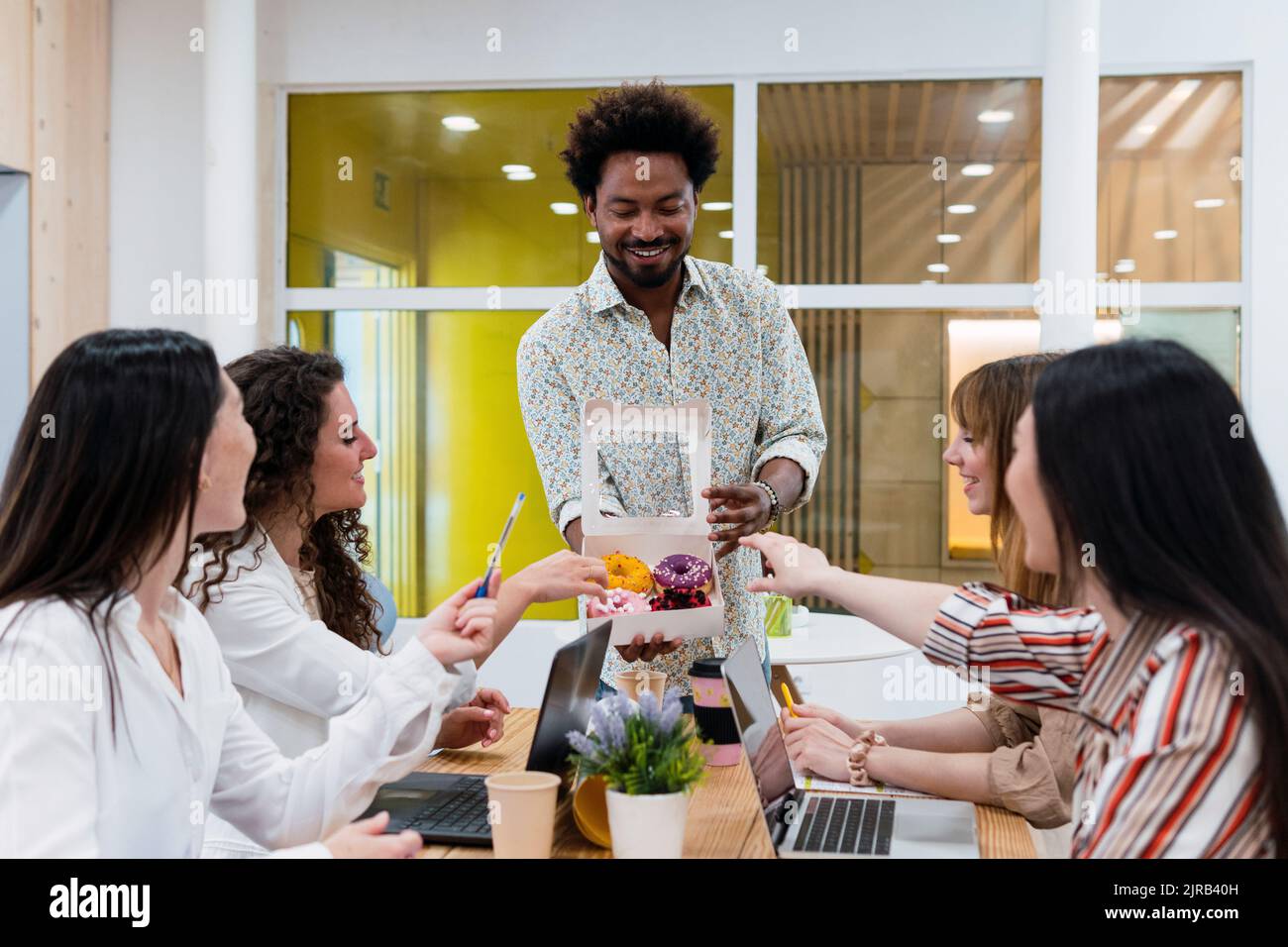 Uomo d'affari che consegna le ciambelle ai colleghi in ufficio Foto Stock