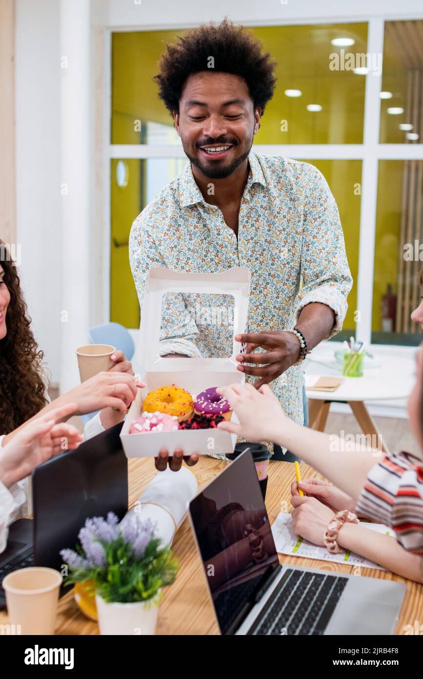 Uomo d'affari che consegna le ciambelle ai colleghi in ufficio Foto Stock