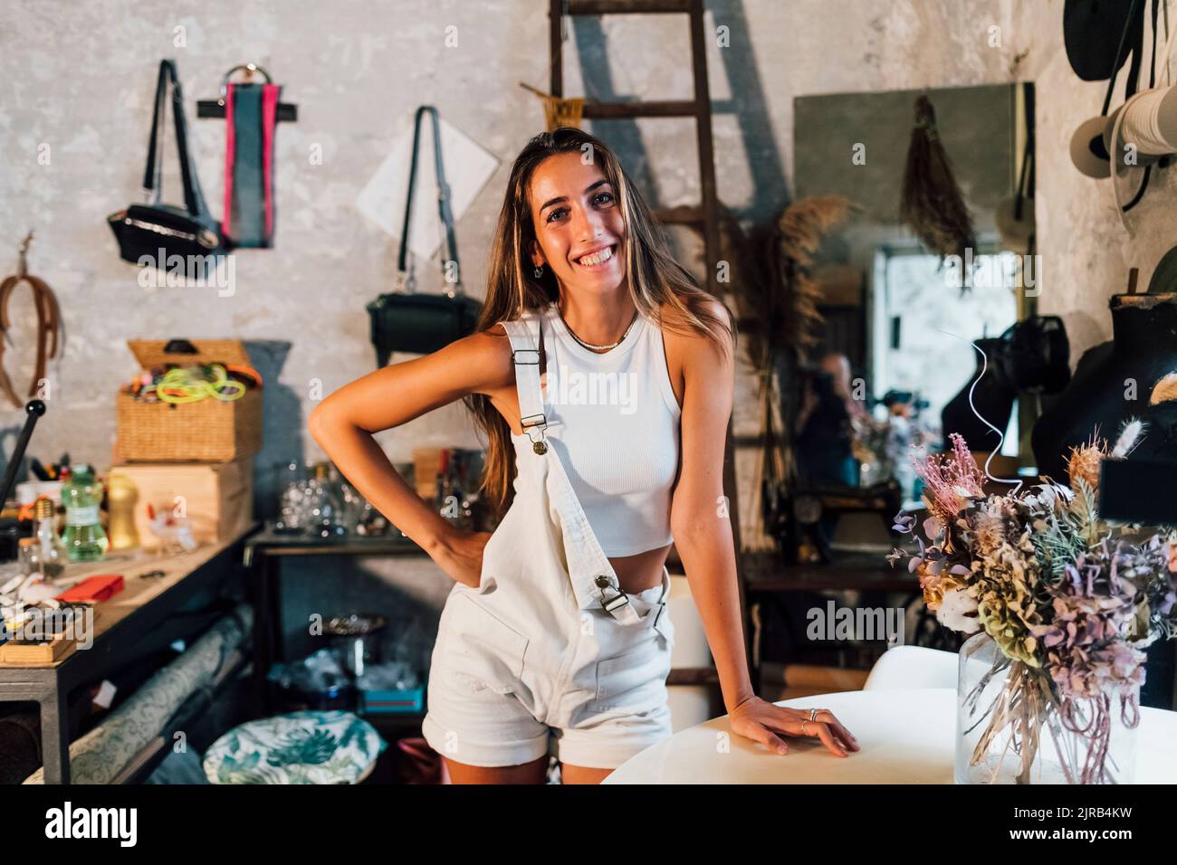 Felice stilista di moda in piedi con mano sul fianco in officina Foto Stock