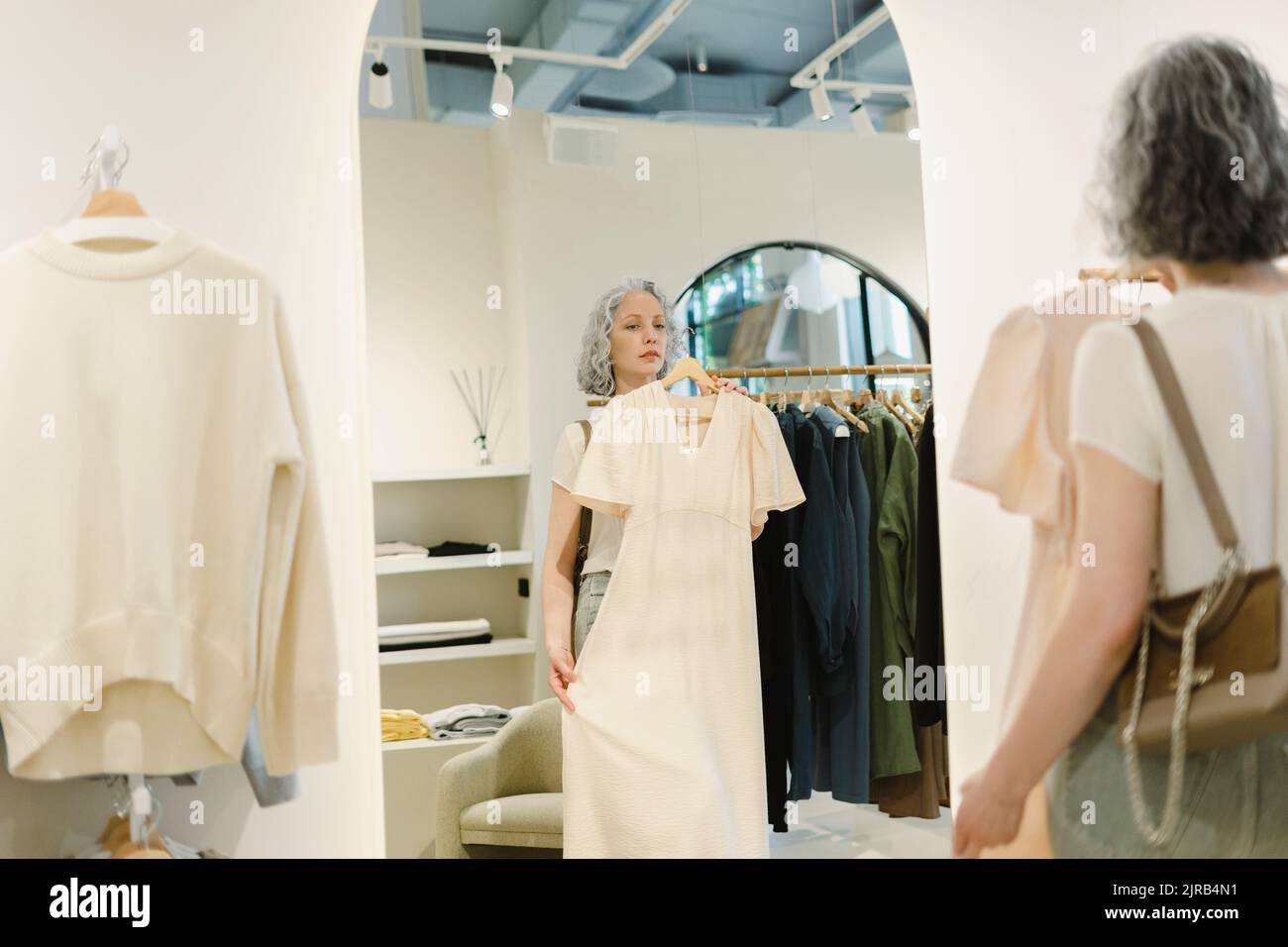 Donna che prova su vestito di fronte allo specchio al negozio Foto Stock