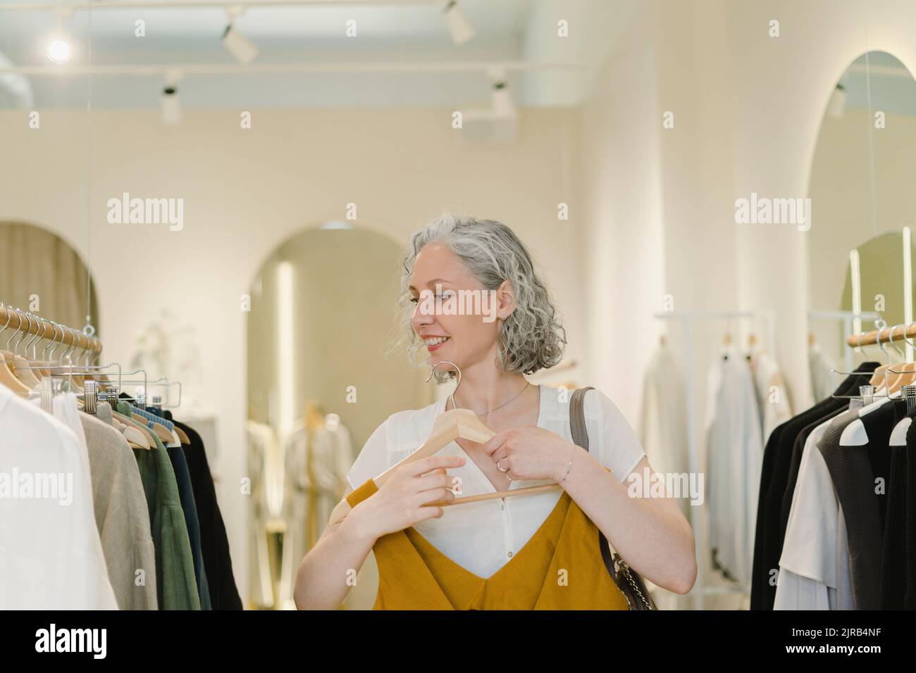 Donna sorridente che tiene l'abito in piedi nel negozio di vestiti Foto Stock