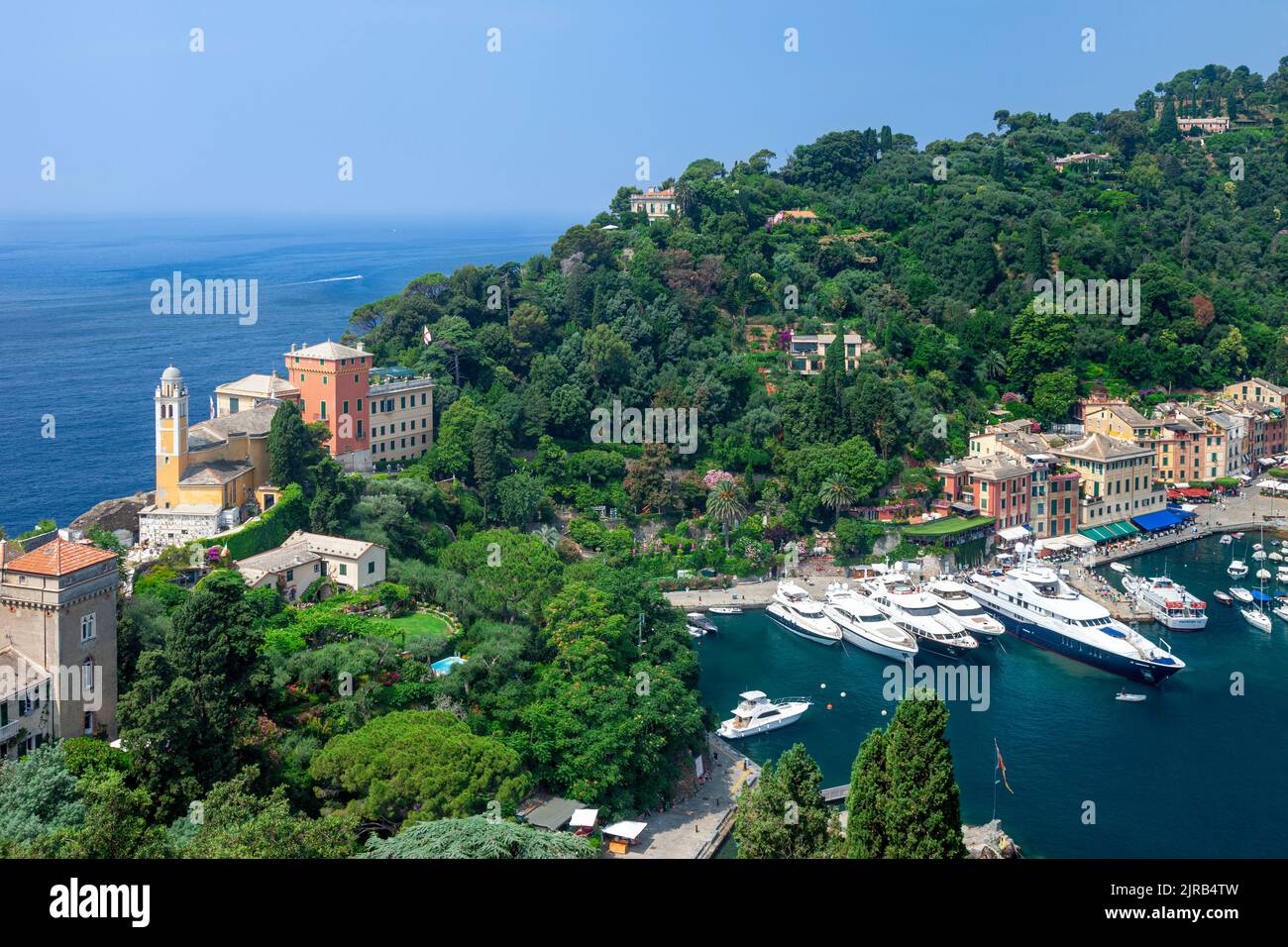 Chiesa San Giorgio, verde collina e barche di lusso ormeggiate nella piccola città portuale di Portofino, Liguria, Italia Foto Stock