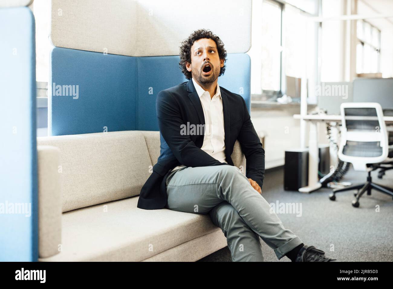 Uomo d'affari che sbadigna seduto sul divano sul posto di lavoro Foto Stock