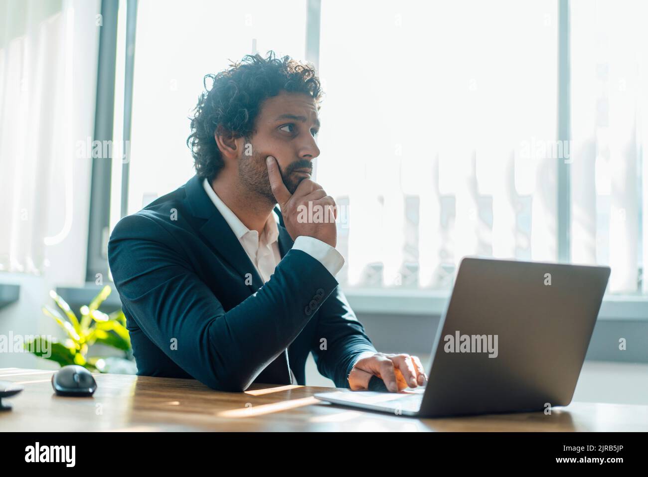 Uomo d'affari contemplativo con computer portatile sulla scrivania sul posto di lavoro Foto Stock