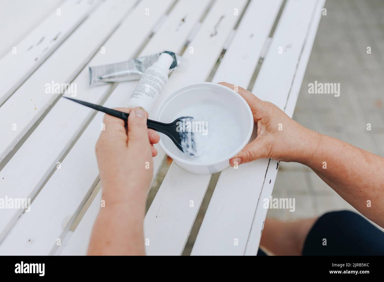 Mani di donna anziana miscelazione tintura capelli in ciotola sul tavolo Foto Stock