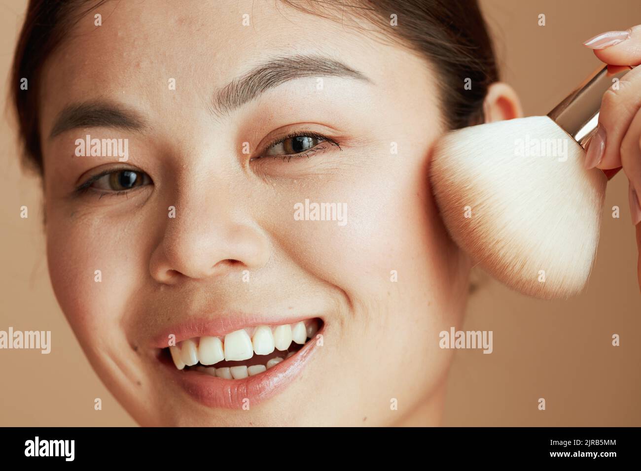 giovane donna asiatica con pennello trucco su sfondo beige. Foto Stock