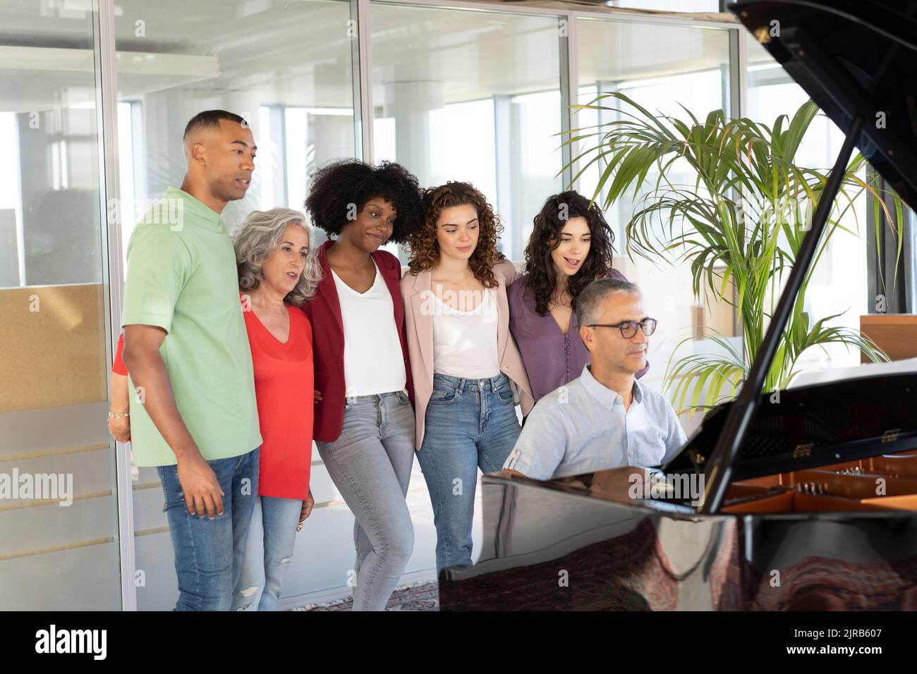 Donne d'affari in piedi con un uomo d'affari che guarda un collega che suona il pianoforte in ufficio Foto Stock