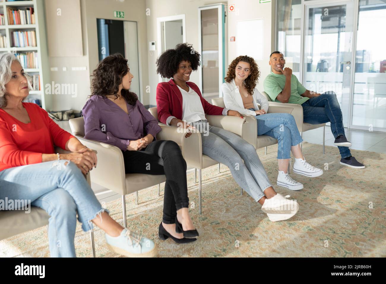 Colleghi che guardano una giovane imprenditrice sorridente che condivide idee in ufficio Foto Stock