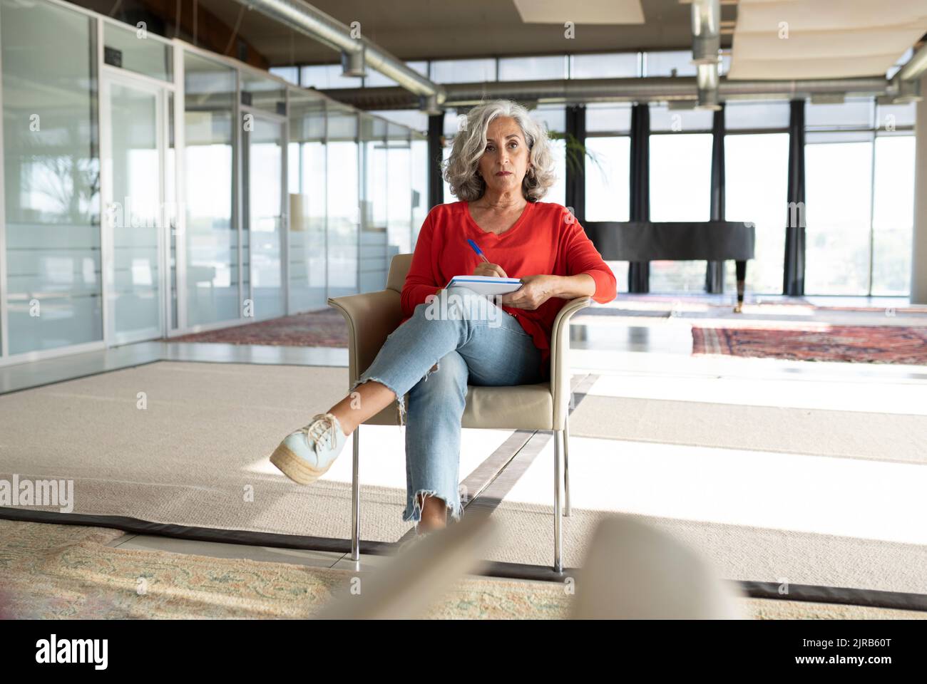 Donna d'affari anziana con gambe incrociate al ginocchio sulla sedia in ufficio Foto Stock