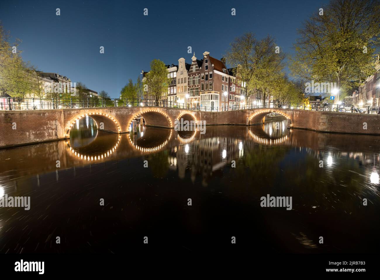 Olanda, Olanda del Nord, Amsterdam, ponte ad arco illuminato che si estende sul canale cittadino di notte Foto Stock
