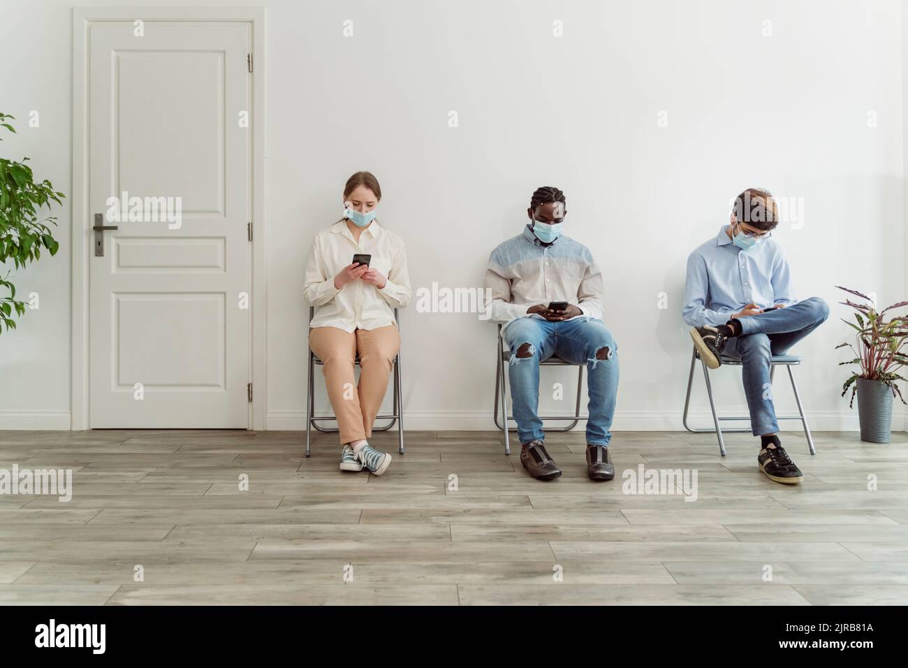 Persone che indossano maschere facciali seduti sulle sedie nell'area di attesa Foto Stock