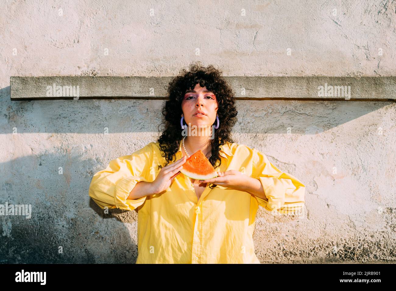 Donna con fettina di anguria davanti al muro Foto Stock